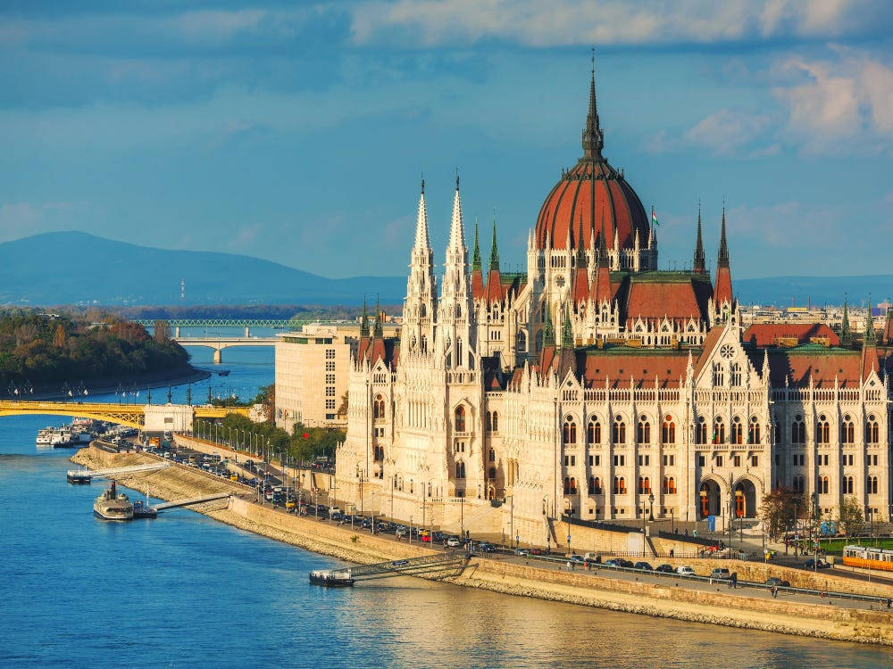 budapest 桌布 壁紙 — 宏偉的匈牙利國會大廈，紅色的屋頂和尖塔，在多瑙河畔部分多雲的天空下雄偉地矗立。