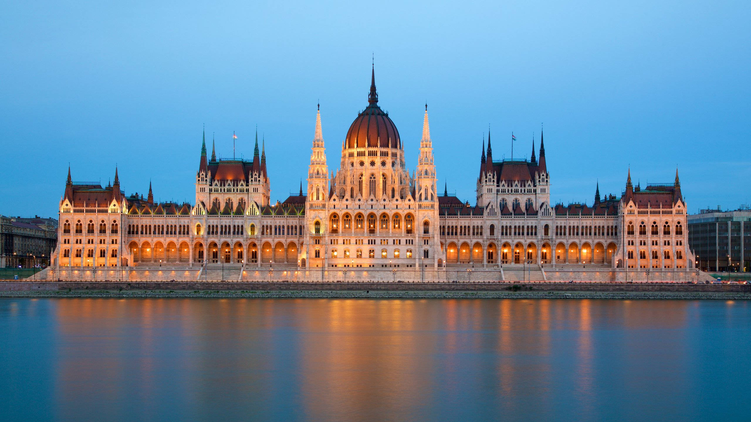 Hungary 桌布 壁紙 — 宏偉的匈牙利國會大廈在黃昏時分亮起燈光，金色的燈光美麗地倒映在平靜的多瑙河上。