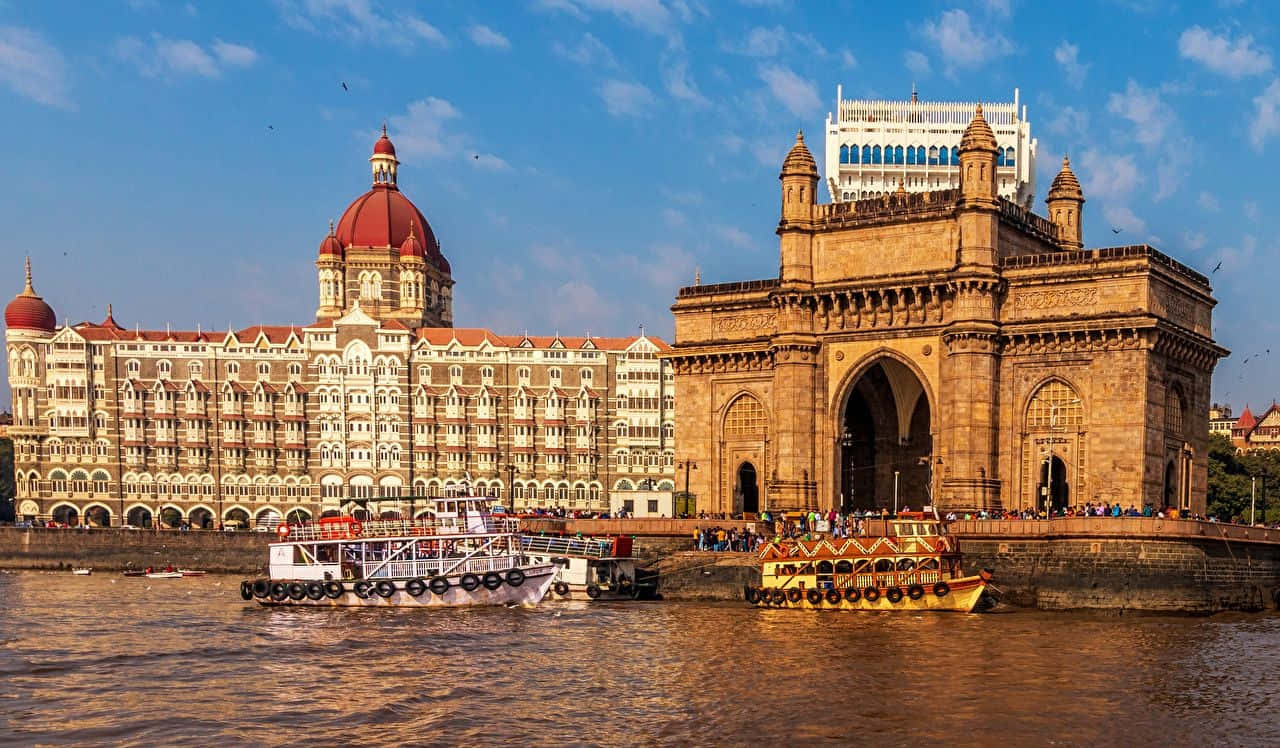 Mumbai 桌布 壁紙 — 宏偉的印度門和泰姬瑪哈酒店在水邊巍然聳立，藍天白雲下，船隻穿梭而過。