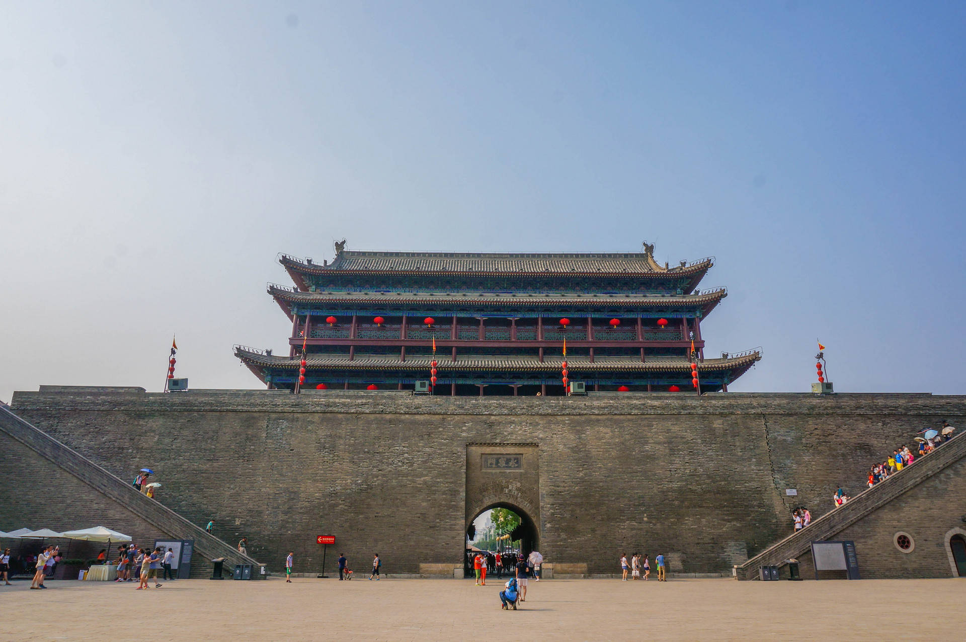 Xian 桌布 壁紙 — 宏偉的古代中國城門，掛著紅燈籠，遊客在石階上，天空清澈湛藍。