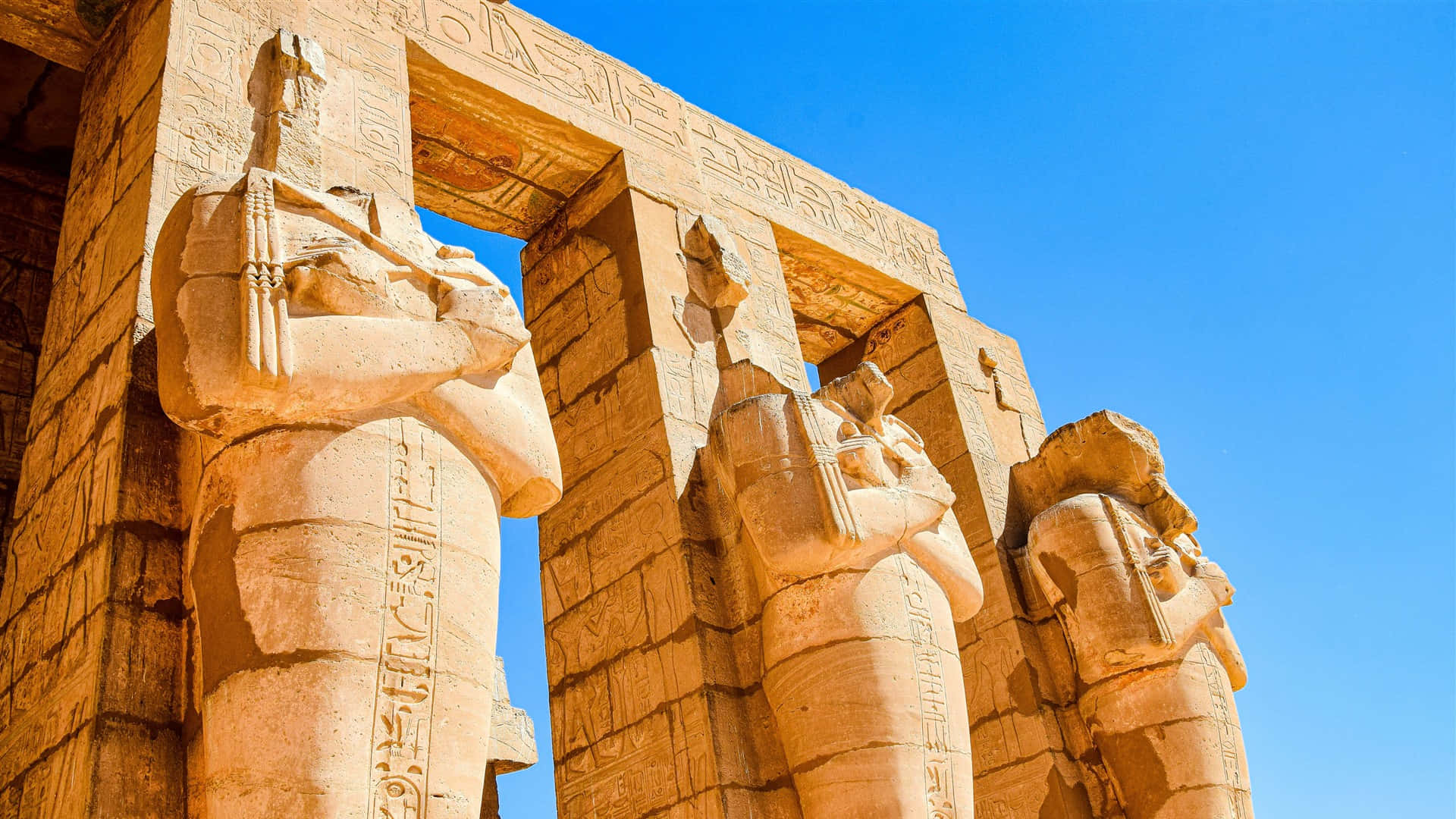 egyptian 桌布 壁紙 — 宏偉的古埃及神廟柱子上刻有象形文字，在清澈的藍天下高高聳立。