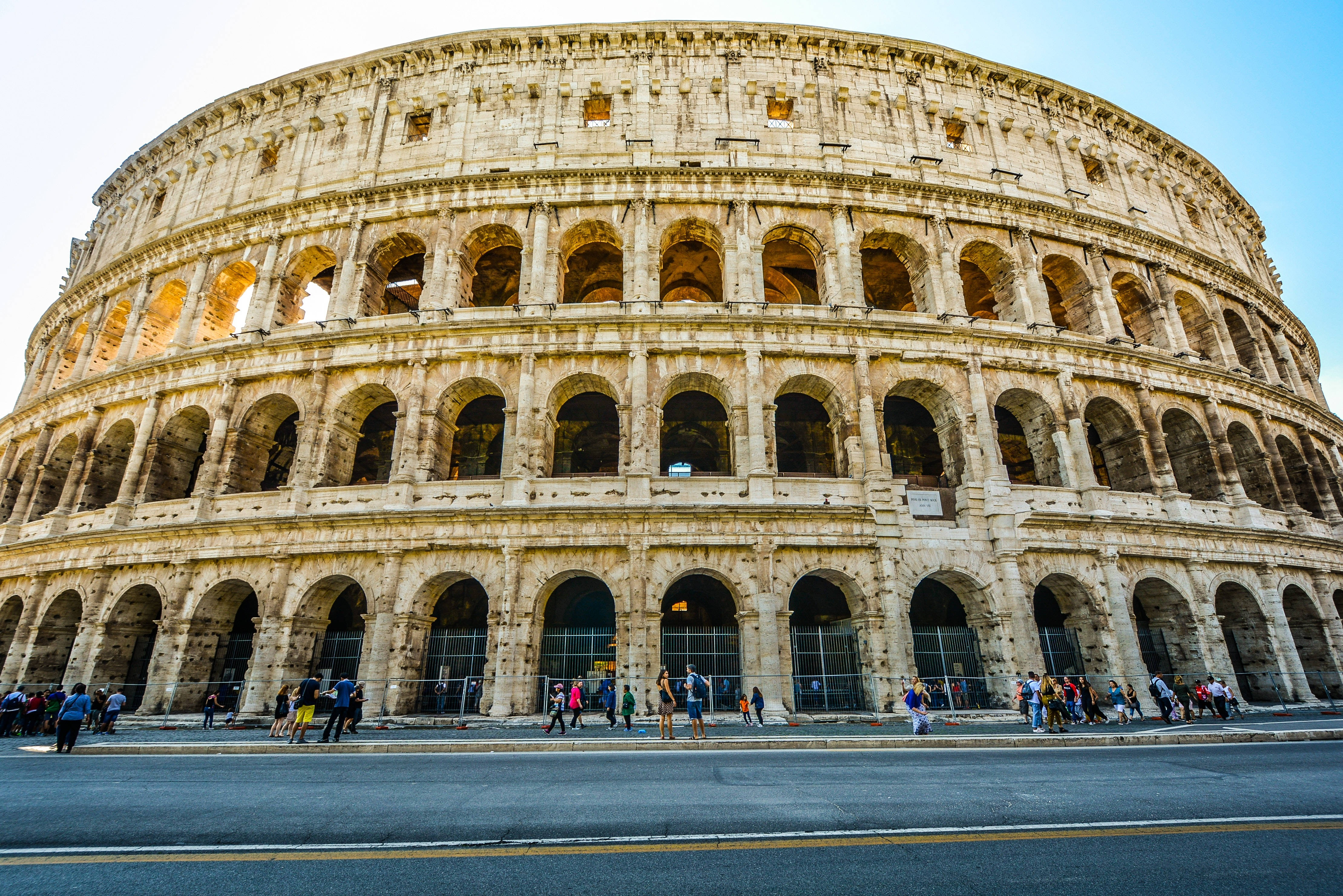 Rome 桌布 壁紙 — 宏偉的古羅馬競技場沐浴在金色的夕陽下，遊客在其巨大的石拱門下漫步。