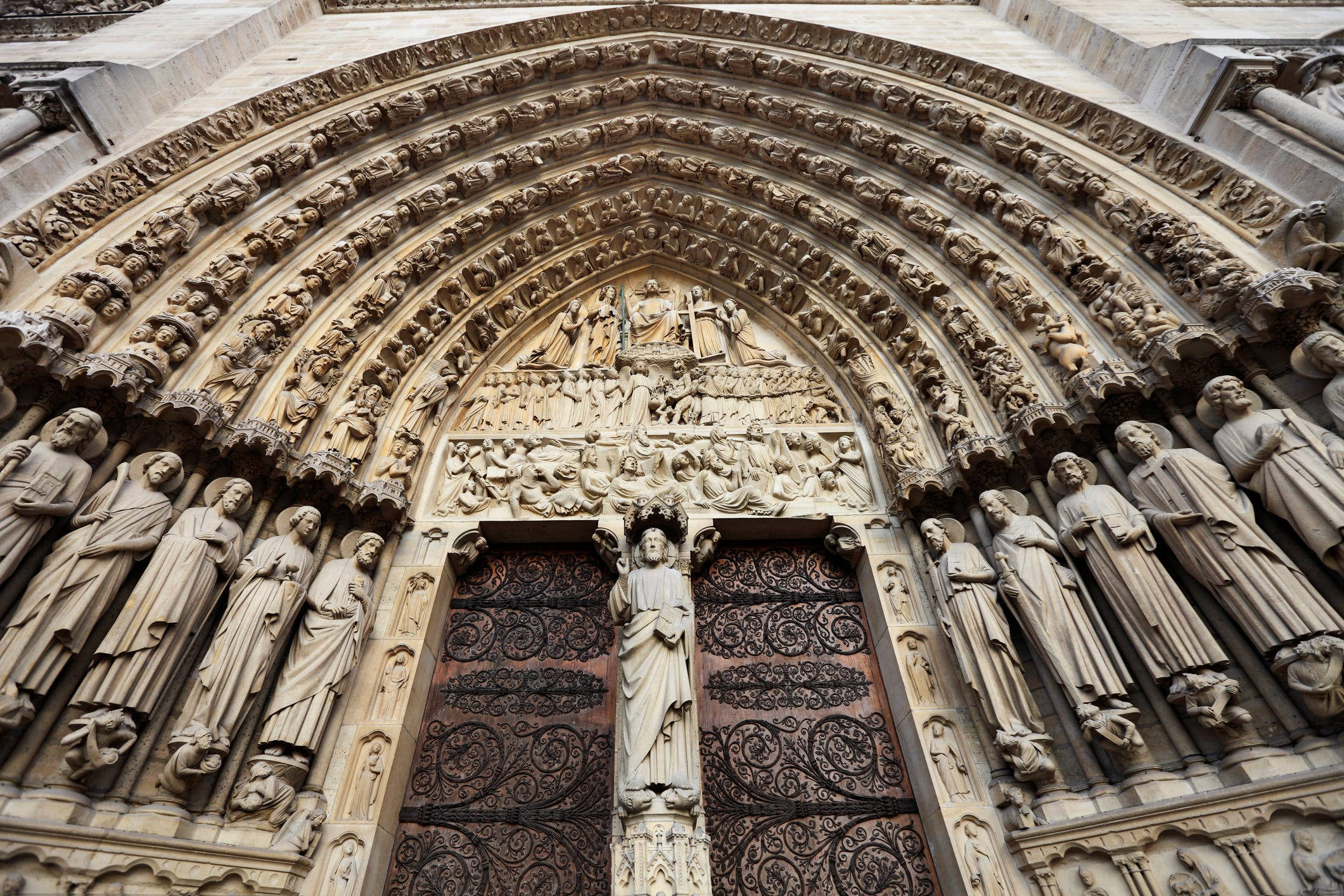 Notre Dame 桌布 壁紙 — 宏偉的哥德式大教堂入口，精緻的石雕和雕像兩旁裝飾著華麗的鐵門。
