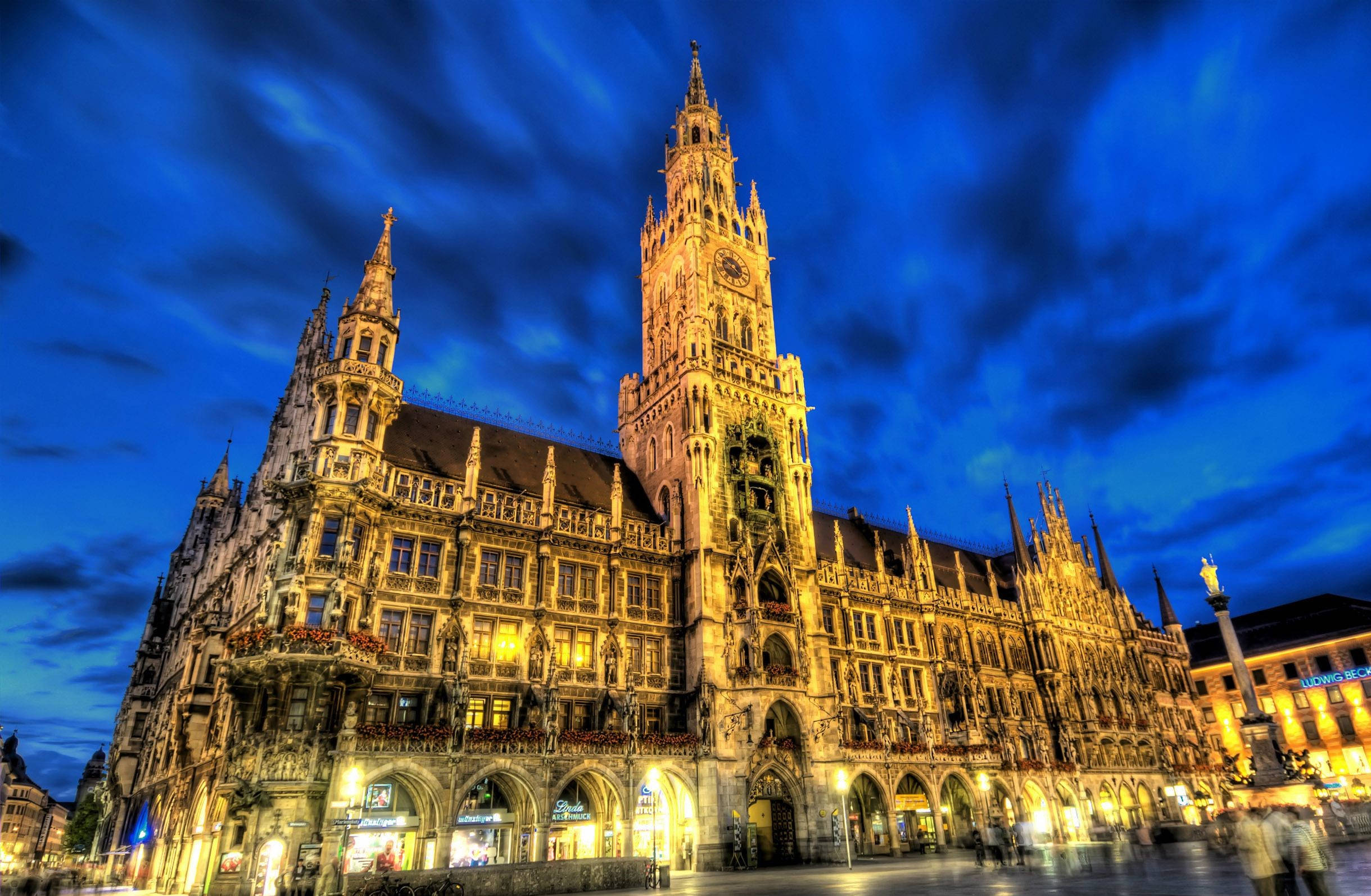 Munich 桌布 壁紙 — 宏偉的哥德式市政廳塔樓在戲劇性的暮色天空和漩渦狀雲彩的映襯下燈火輝煌。