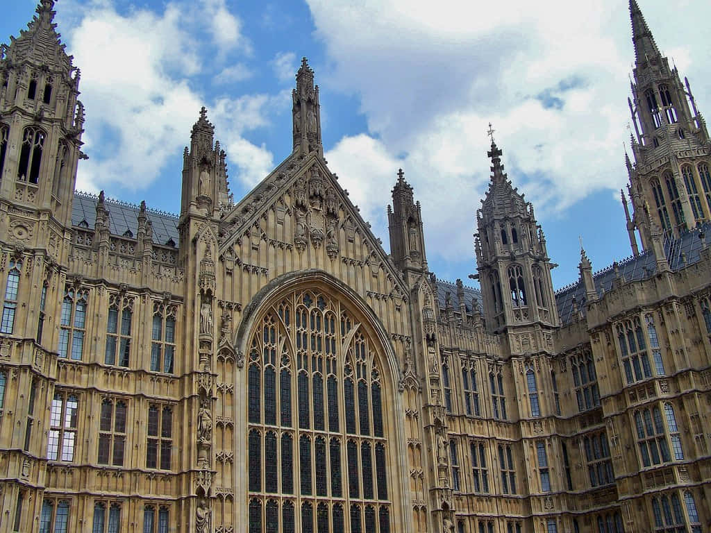 House Of Parliament 桌布 壁紙 — 宏偉的哥德式建築，擁有複雜的尖塔和彩色玻璃窗，在明亮的藍天和白雲下。