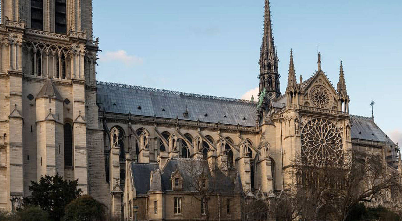 Notre Dame 桌布 壁紙 — 宏偉的哥德式聖母院，擁有精緻的石砌外牆、玫瑰窗和尖塔，在清澈的藍天下。