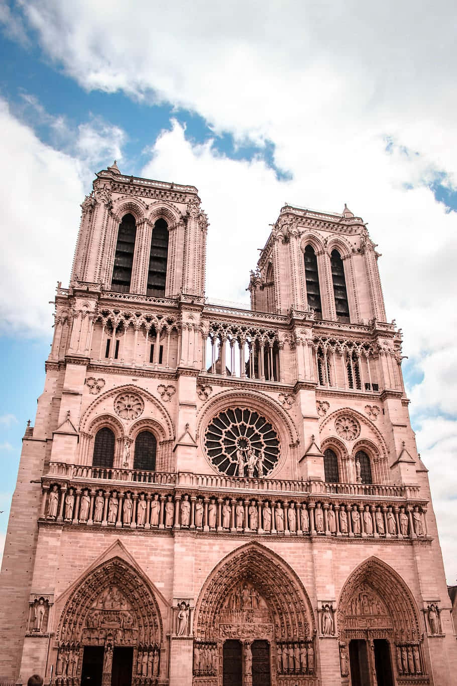 Notre Dame 桌布 壁紙 — 宏偉的哥德式聖母院大教堂，在部分多雲的藍天下，以精緻的石雕和雙塔雄偉地聳立。