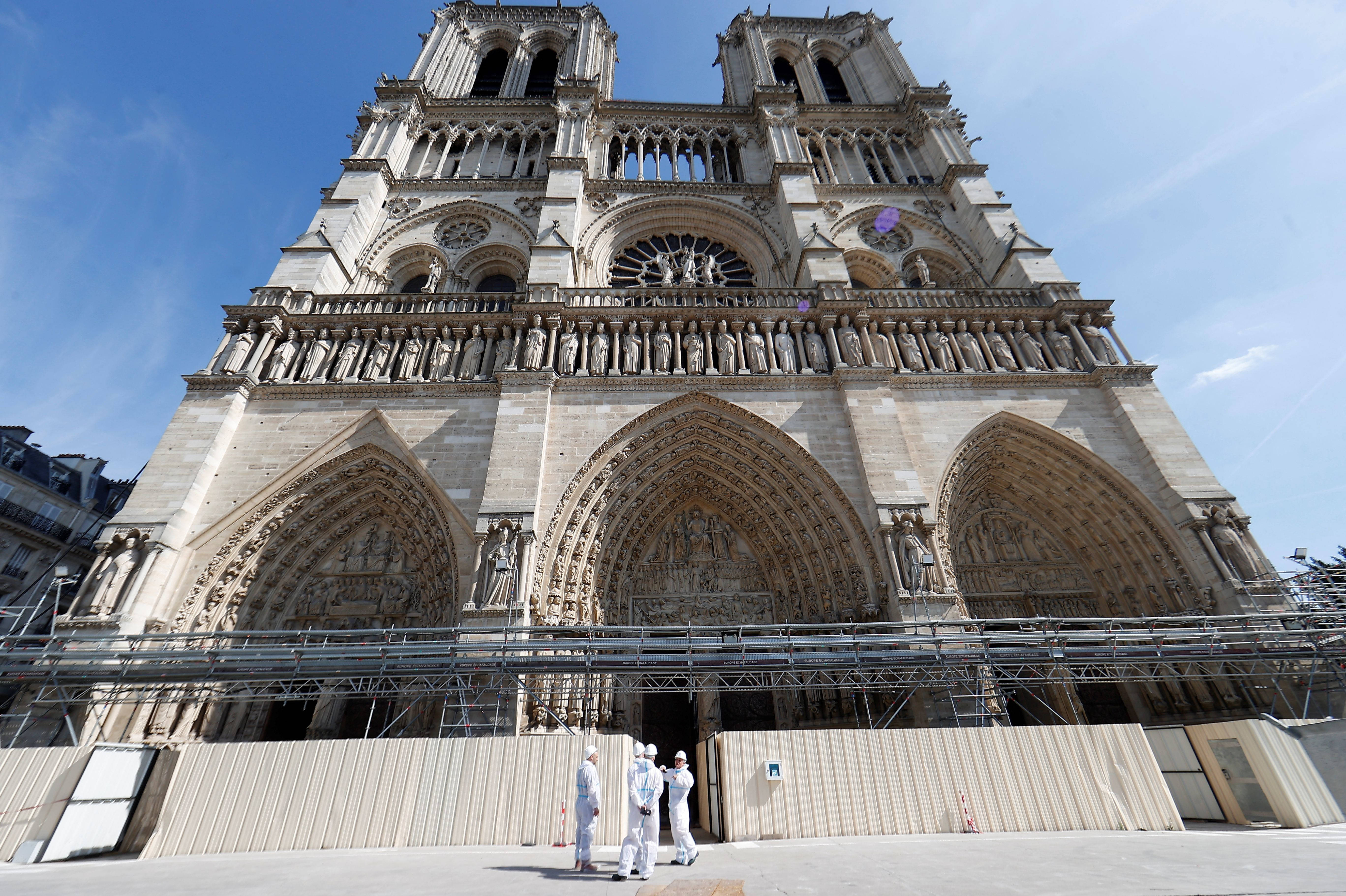 Notre Dame 桌布 壁紙 — 宏偉的哥德式聖母院大教堂在藍天下，附近有穿著白色工作服的工人在鷹架上。