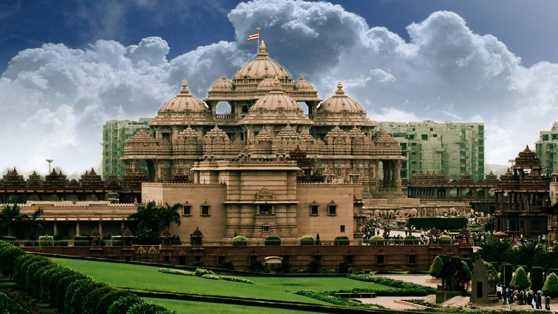 Delhi 桌布 壁紙 — 宏偉的圓頂寺廟建築群，雕刻精美，在戲劇性的多雲天空和現代建築背景下巍然聳立。