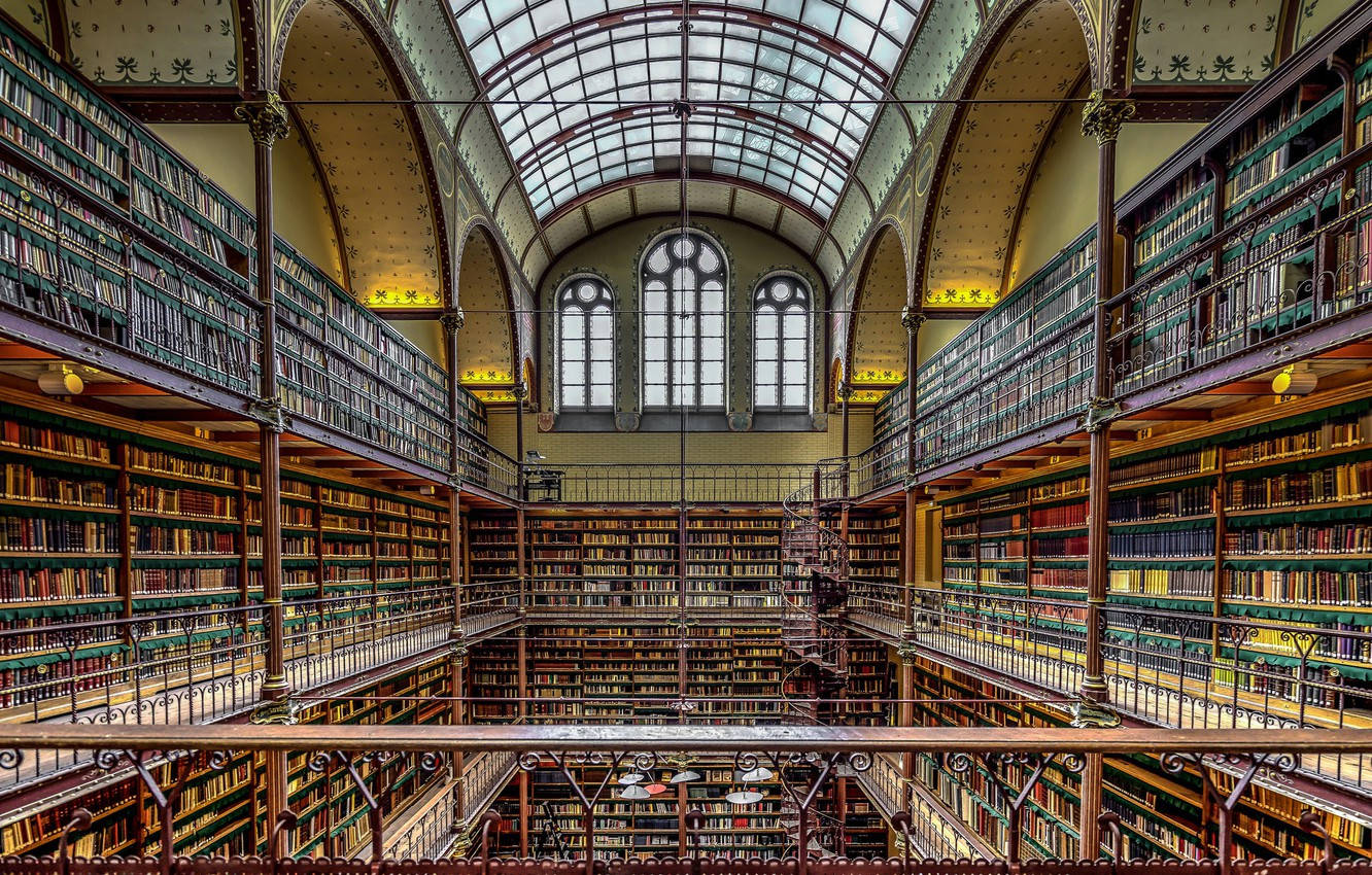 Library 桌布 壁紙 — 宏偉的多層圖書館，擁有華麗的鐵藝書架，上方是玻璃穹頂天花板，沐浴在自然光中。