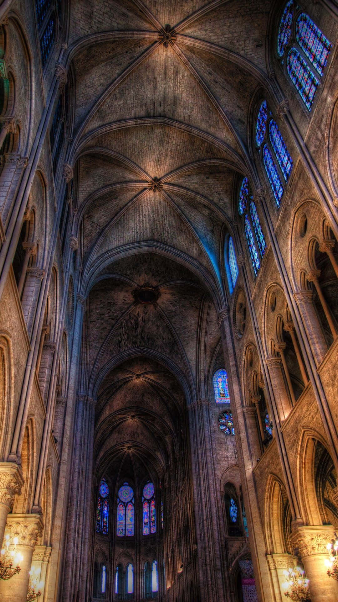 Notre Dame 桌布 壁紙 — 宏偉的大教堂內部，擁有高聳的石拱頂和彩色玻璃窗，投射出五彩斑斕的光線。