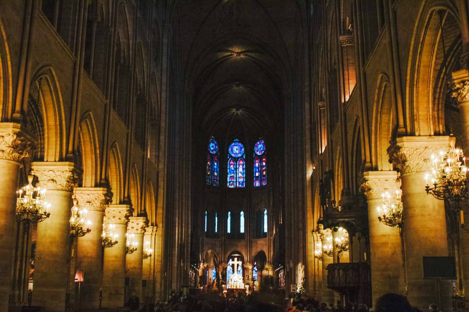Notre Dame 桌布 壁紙 — 宏偉的大教堂內部，沐浴在吊燈和彩色玻璃窗散發的溫暖金色光芒中。