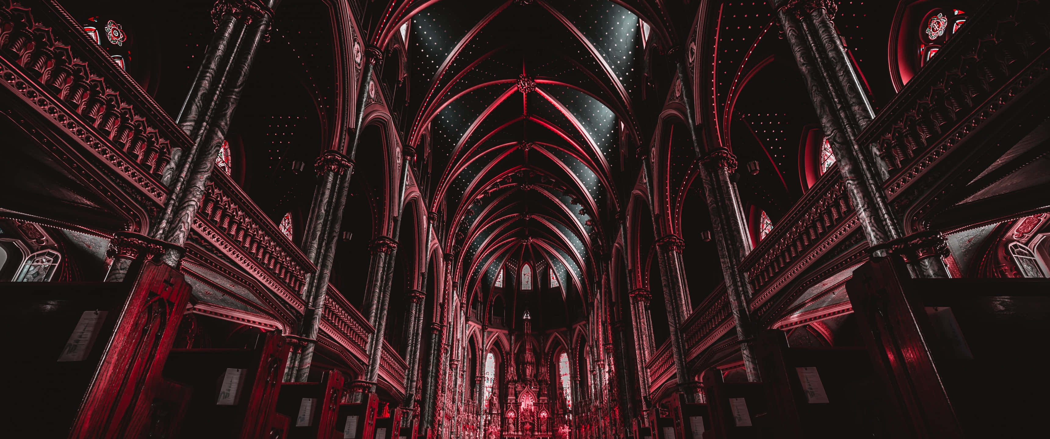Notre Dame 桌布 壁紙 — 宏偉的大教堂內部沐浴在戲劇性的紅光中，突顯了複雜的哥德式拱門和拱形天花板。