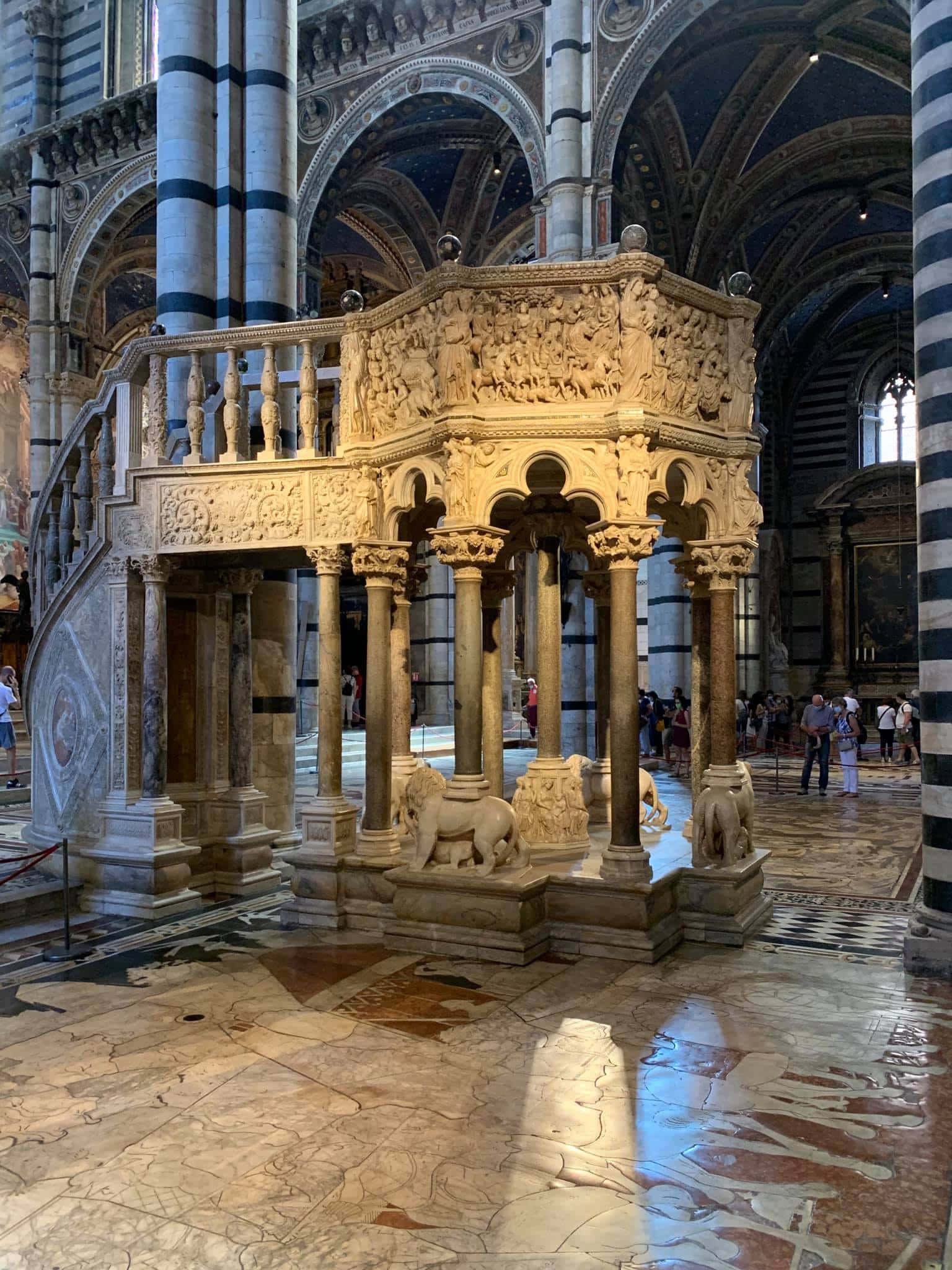 Siena Cathedral 桌布 壁紙 — 宏偉的大理石講道壇，帶有精緻雕刻和獅子雕像，矗立在擁有條紋柱和拱形天花板的教堂內。