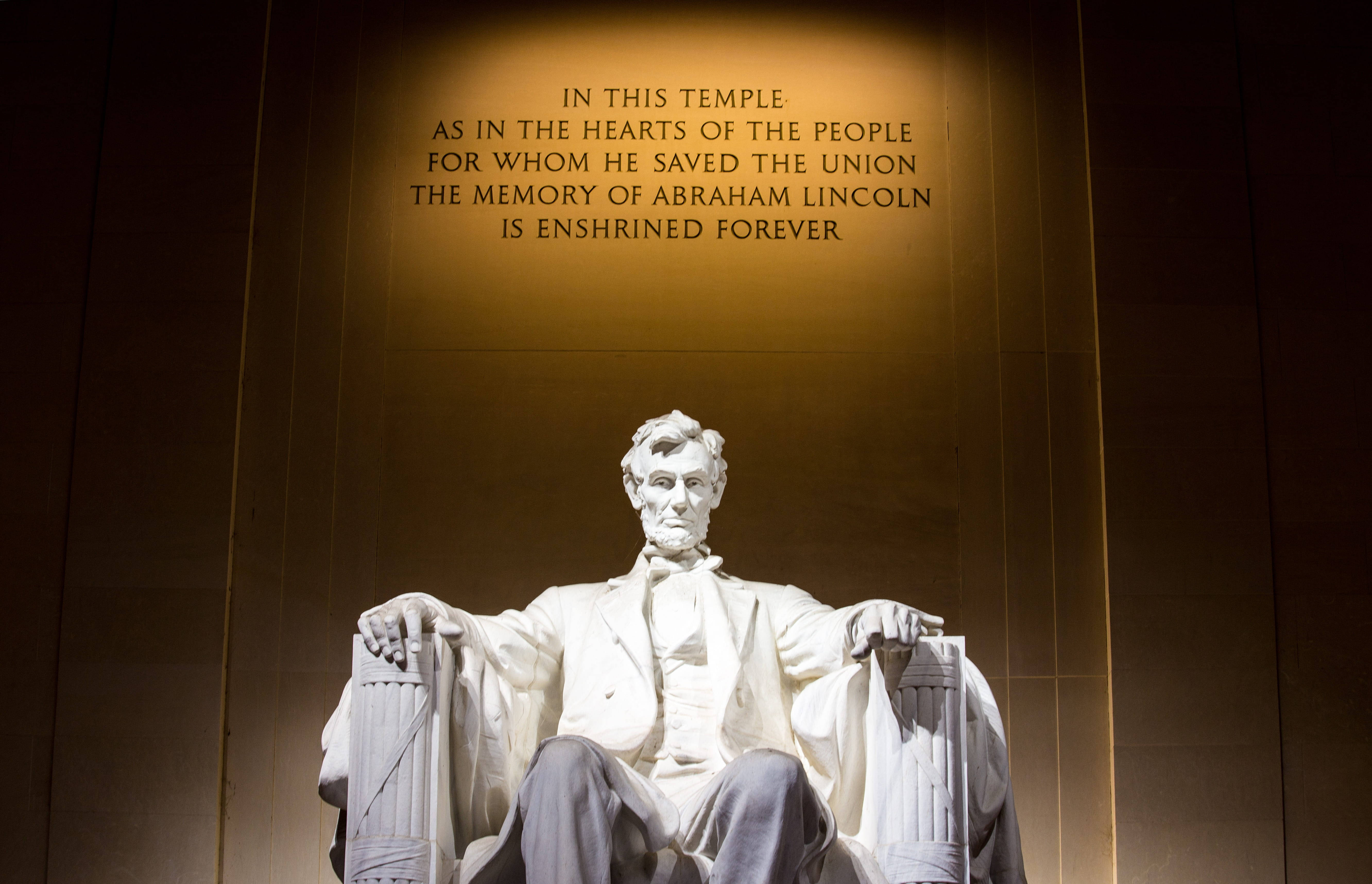 Washington 桌布 壁紙 — 宏偉的大理石雕像，亞伯拉罕·林肯莊嚴地坐在溫暖的聚光燈下，上方刻有紀念文字。