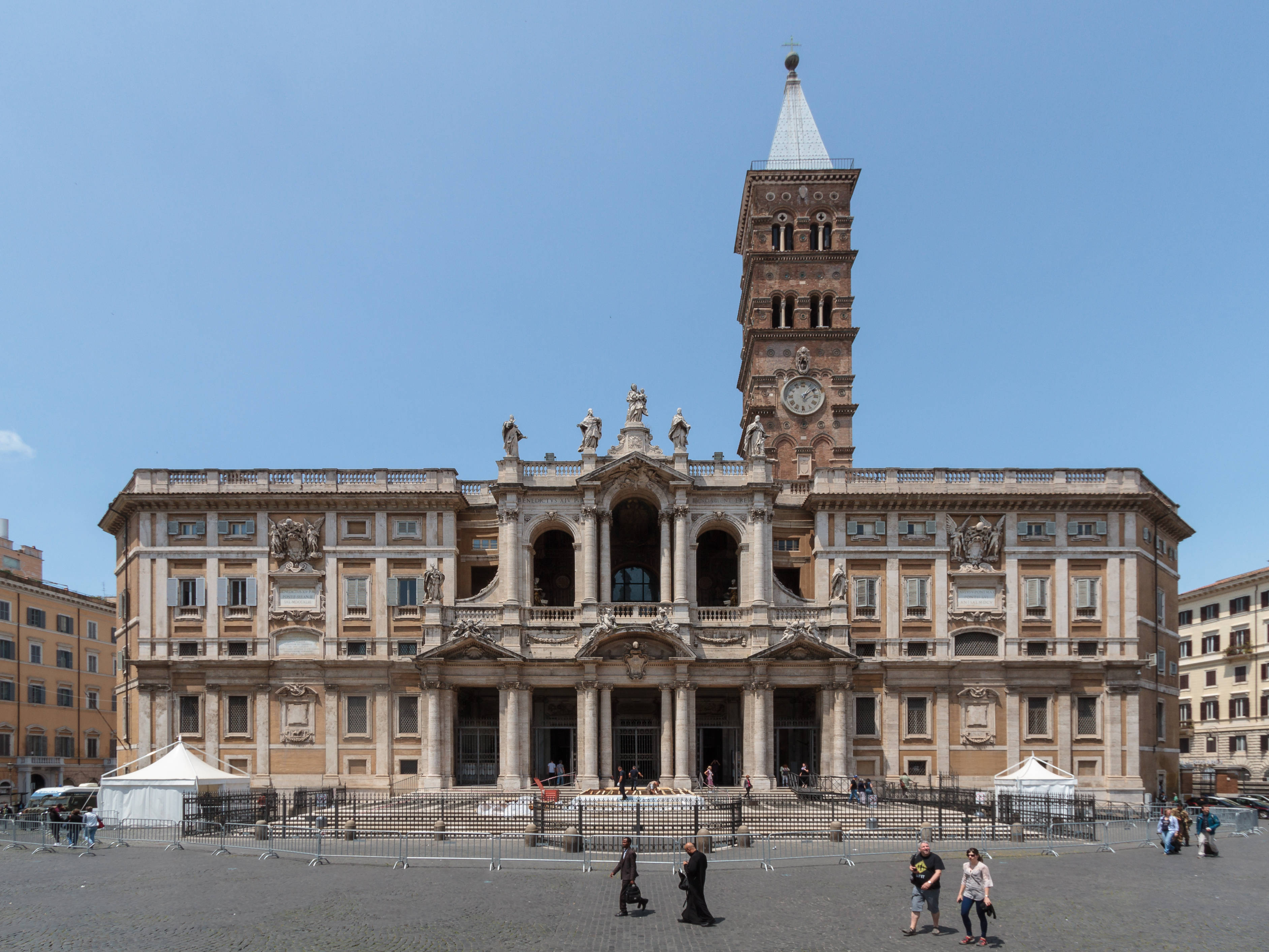 Rome 桌布 壁紙 — 宏偉的巴洛克式教堂，擁有華麗的外牆和高聳的鐘樓，矗立在晴朗的藍天下，人們在開闊的廣場上漫步。
