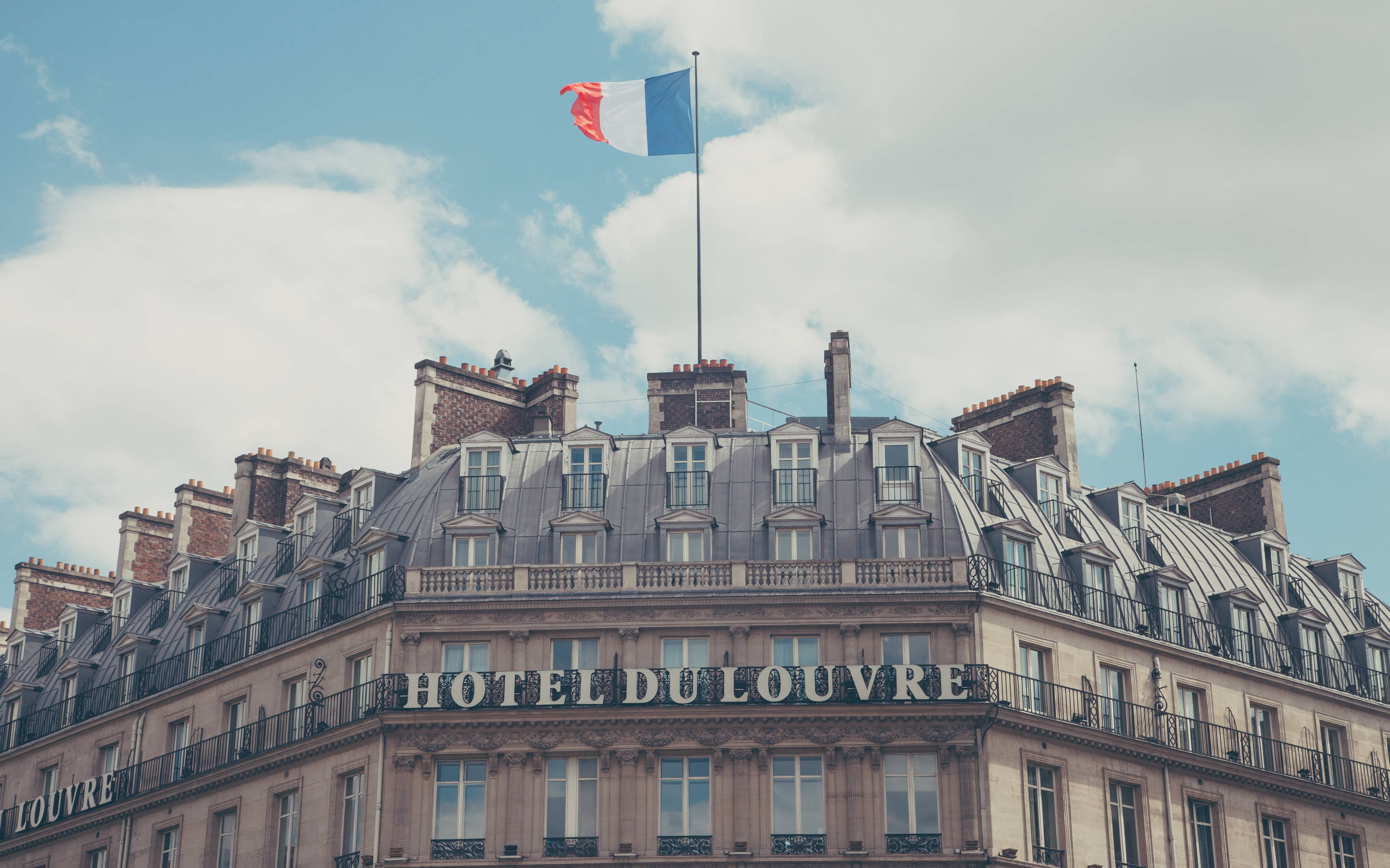 France Flag 桌布 壁紙 — 宏偉的巴黎飯店，法國國旗在其華麗的屋頂上飄揚，天空部分多雲。