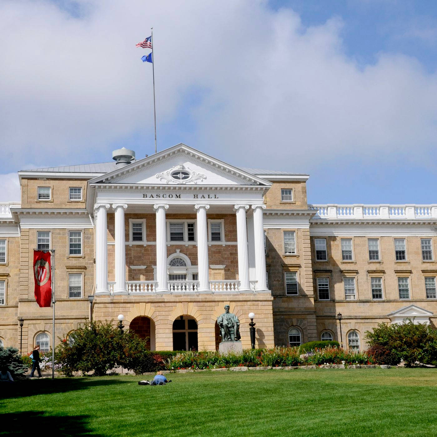 桌布 壁紙 — 宏偉的新古典主義Bascom Hall，白色柱子和旗幟矗立在部分多雲的天空下，周圍是修剪整齊的草坪和雕像。