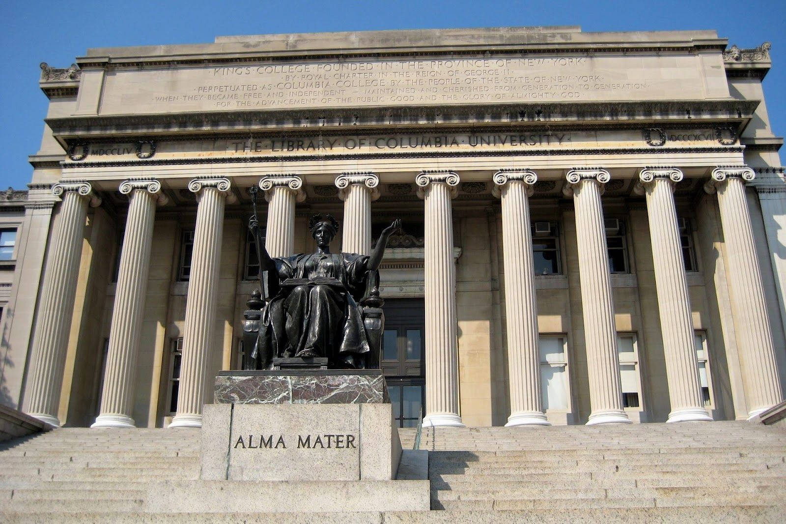 Library 桌布 壁紙 — 宏偉的新古典主義圖書館外牆，高聳的柱子和青銅Alma Mater雕像在白色大理石台階上，背景是清澈的藍天。