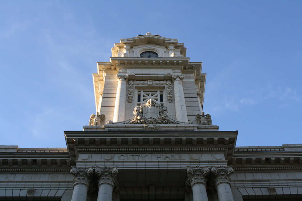 Clock 桌布 壁紙 — 宏偉的新古典主義市政廳塔樓，飾有華麗的柱子和時鐘，襯托著清澈的藍天。