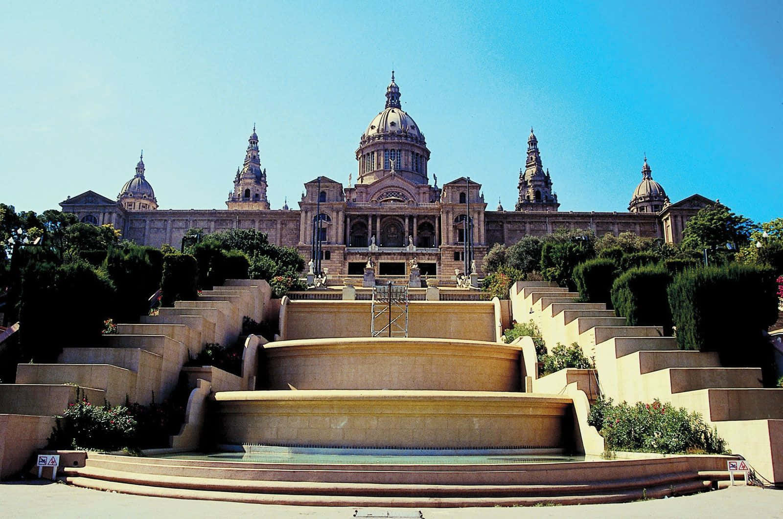 Barcelona 桌布 壁紙 — 宏偉的新古典主義建築，擁有圓頂和塔樓，在寬闊的石階和噴泉後方，在清澈的藍天下聳立。