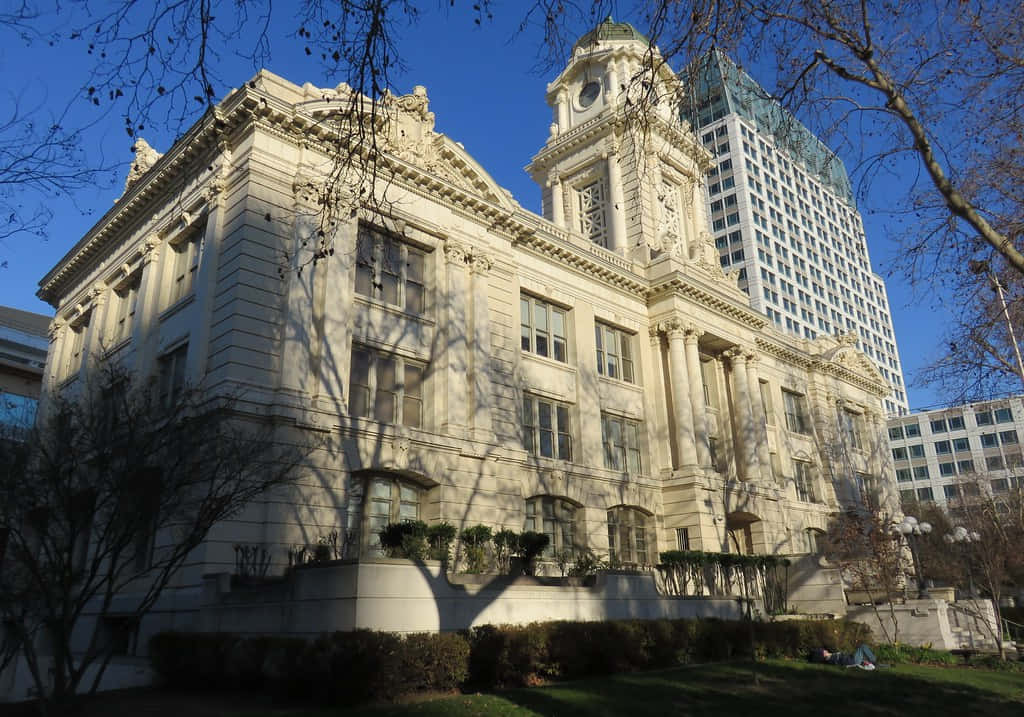 建築 桌布 壁紙 — 宏偉的新古典主義法院，帶有華麗的柱子和鐘樓，矗立在現代玻璃摩天大樓旁，天空清澈湛藍。