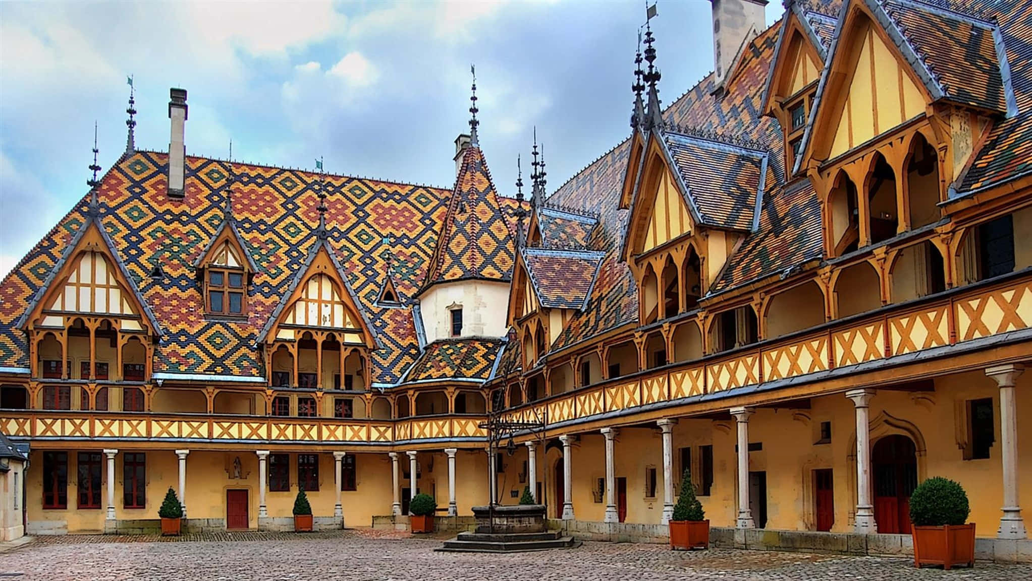 France 桌布 壁紙 — 宏偉的歷史庭院，擁有華麗的黃色和紅色瓷磚屋頂，在陰天之下。