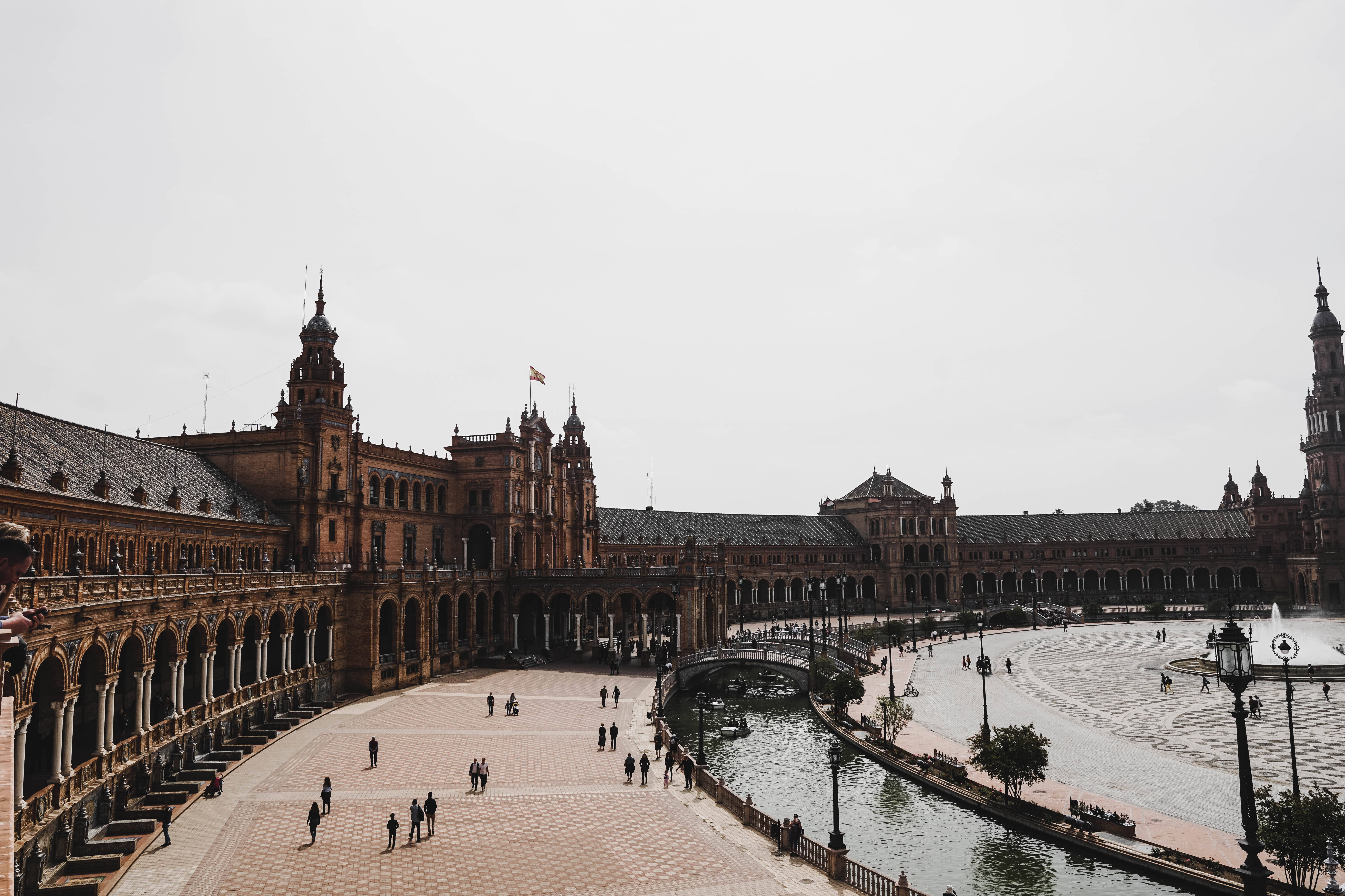 Seville 桌布 壁紙 — 宏偉的歷史廣場，擁有華麗建築和中央運河，天空多雲。