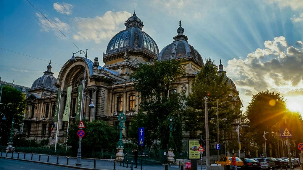 Romania 桌布 壁紙 — 宏偉的歷史建築，圓頂屋頂沐浴在金色夕陽的光芒中，穿過戲劇性的雲層。