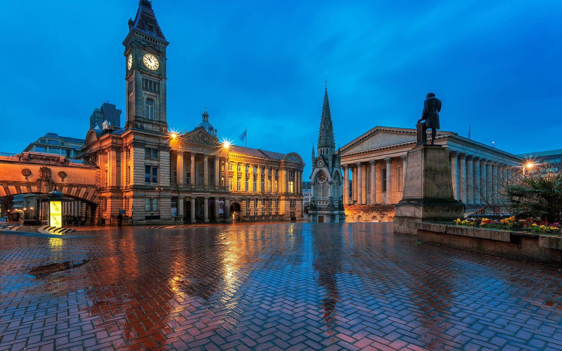Birmingham 桌布 壁紙 — 宏偉的歷史建築物，帶有鐘樓和雕像，在濕漉漉的鵝卵石廣場上反射的暮色天空中溫暖地發光。