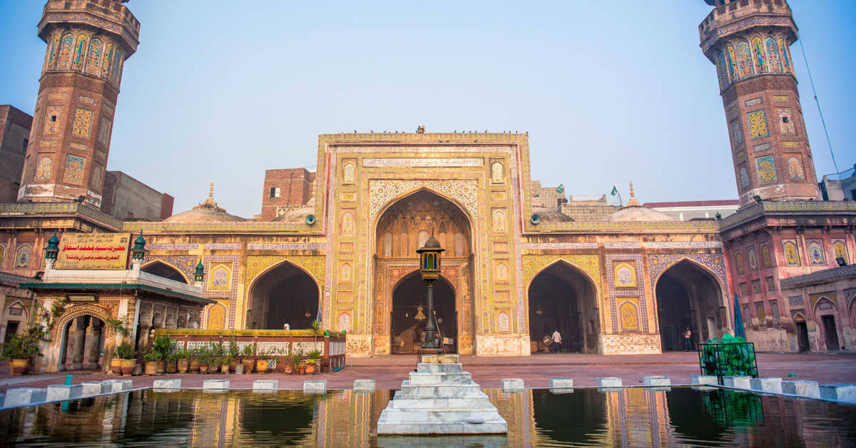 Lahore 桌布 壁紙 — 宏偉的歷史清真寺，裝飾華麗的宣禮塔和拱形大門倒映在中央噴泉中，背景是清澈的藍天。