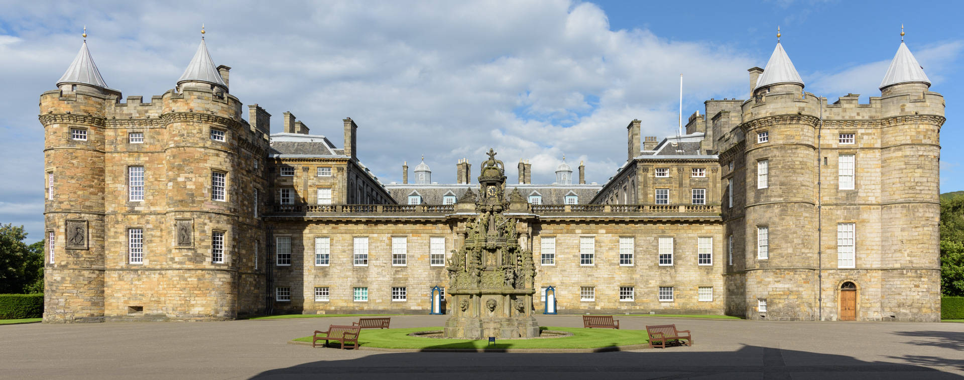 England 桌布 壁紙 — 宏偉的歷史石城堡，設有塔樓和中央噴泉，天空部分多雲。