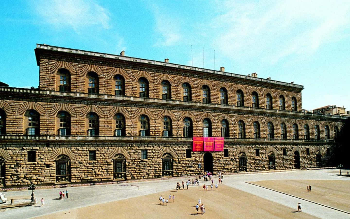 建築 桌布 壁紙 — 宏偉的歷史石建築，擁有拱形窗戶，在晴朗藍天和零星白雲下。