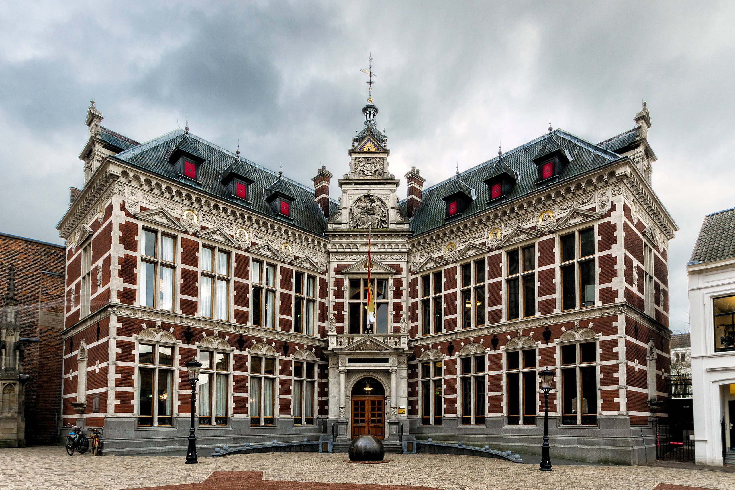 Netherlands 桌布 壁紙 — 宏偉的歷史磚砌建築，帶有華麗的白色石雕細節和紅色老虎窗，天空多雲。