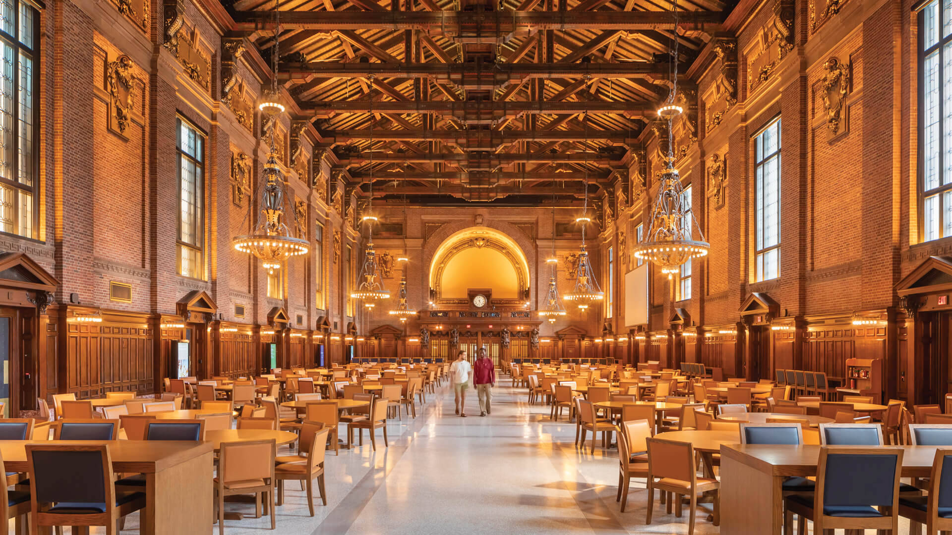 Library 桌布 壁紙 — 宏偉的歷史餐廳，高木樑，溫暖的燈光，兩個人沿著中央走道行走。