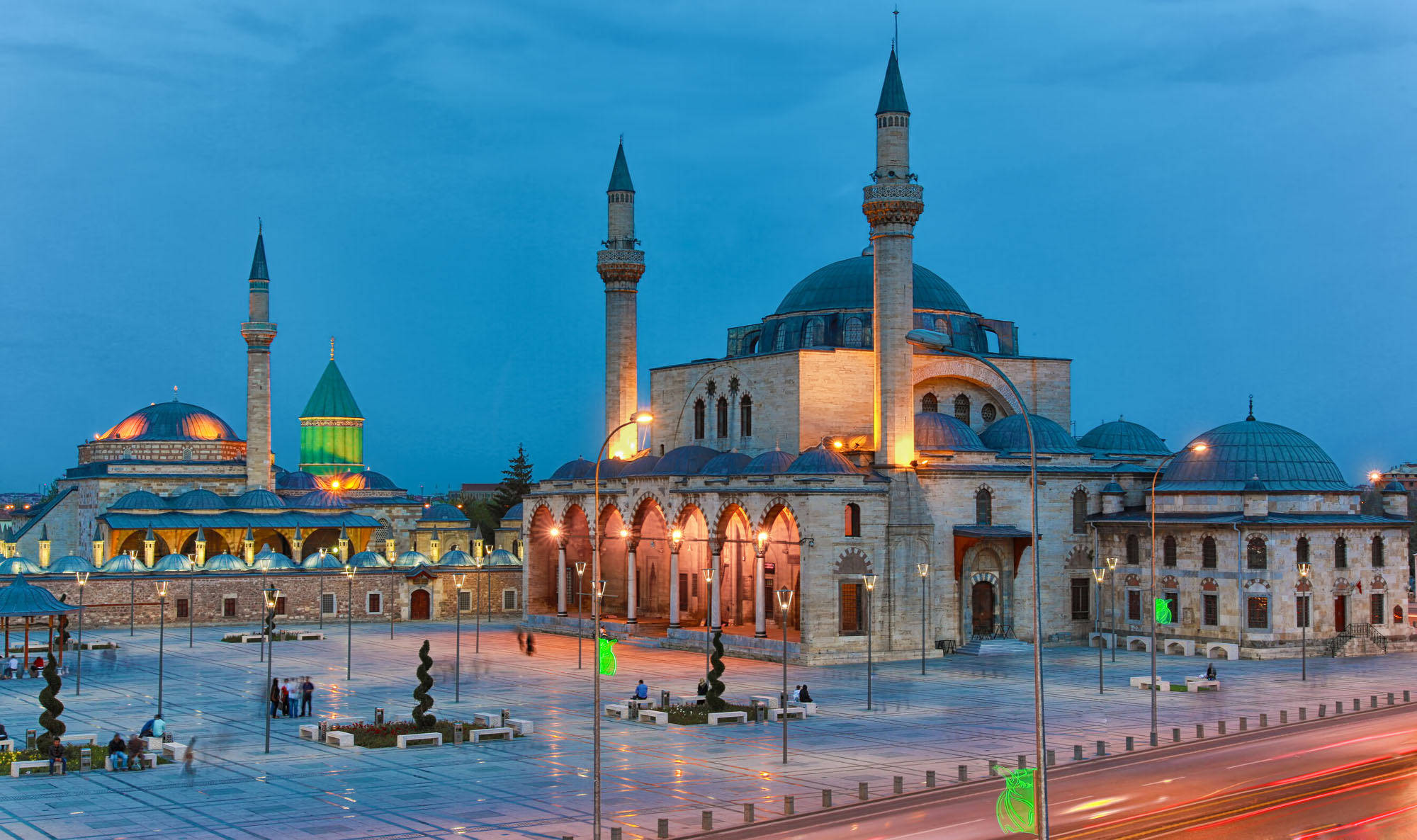 Konya 桌布 壁紙 — 宏偉的照明清真寺建築群，圓頂和宣禮塔在濕漉漉的廣場上空的暮色天空中閃耀。