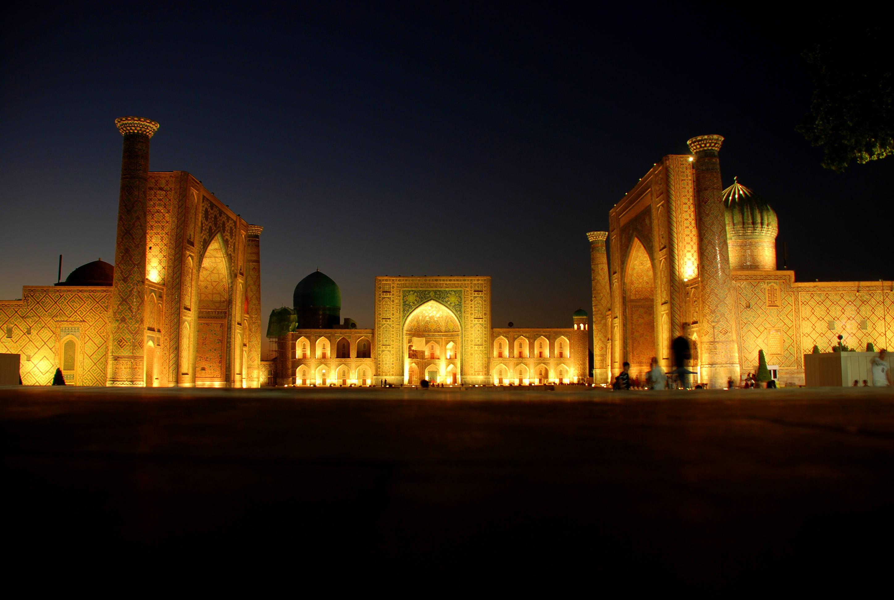 Uzbekistan 桌布 壁紙 — 宏偉的燈光伊斯蘭建築在深沉的暮色天空下溫暖地發光，下方有剪影般的遊客。