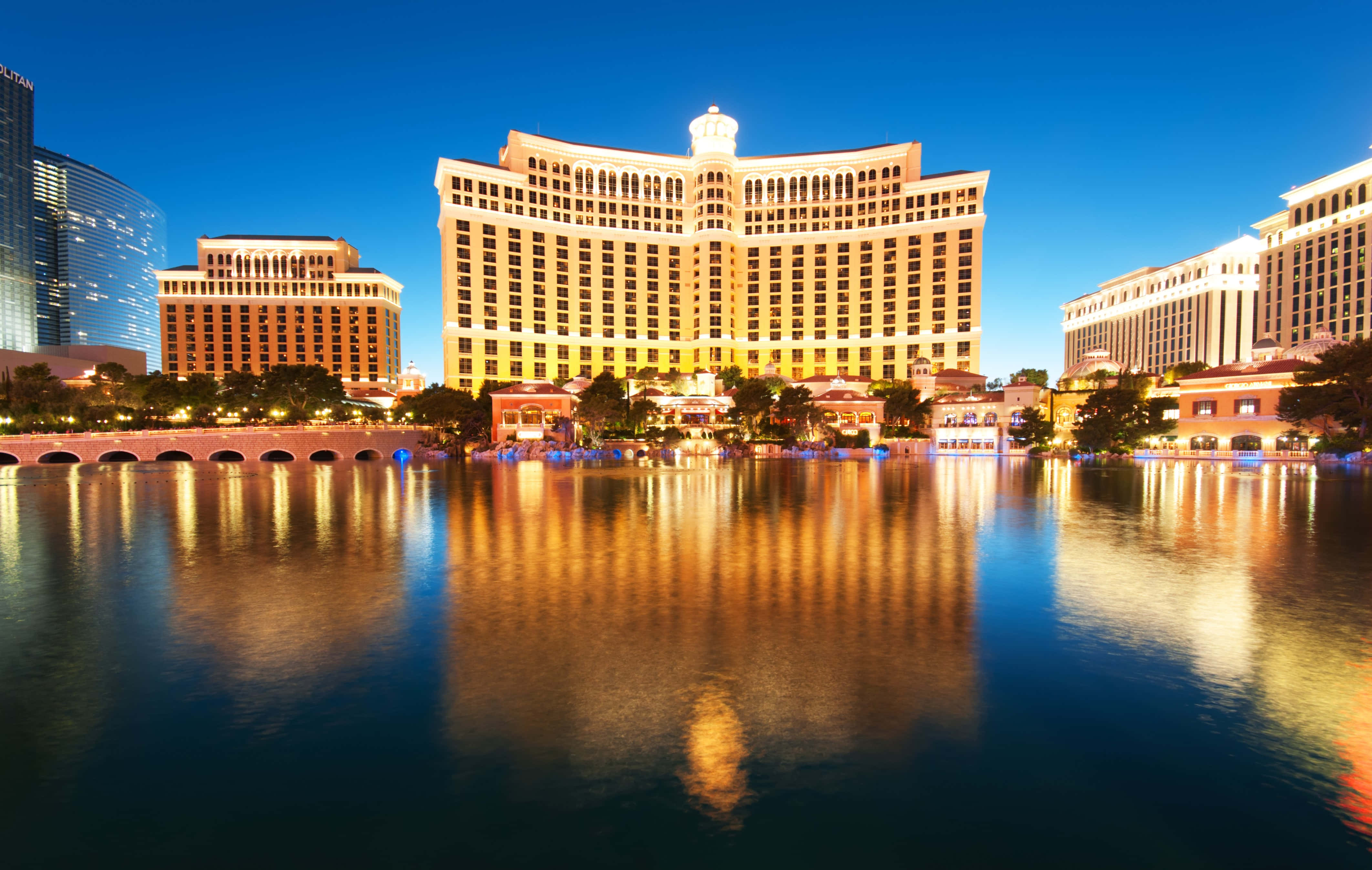 4K Las Vegas 桌布 壁紙 — 宏偉的燈光酒店大樓在暮色天空下倒映在平靜的水面上。