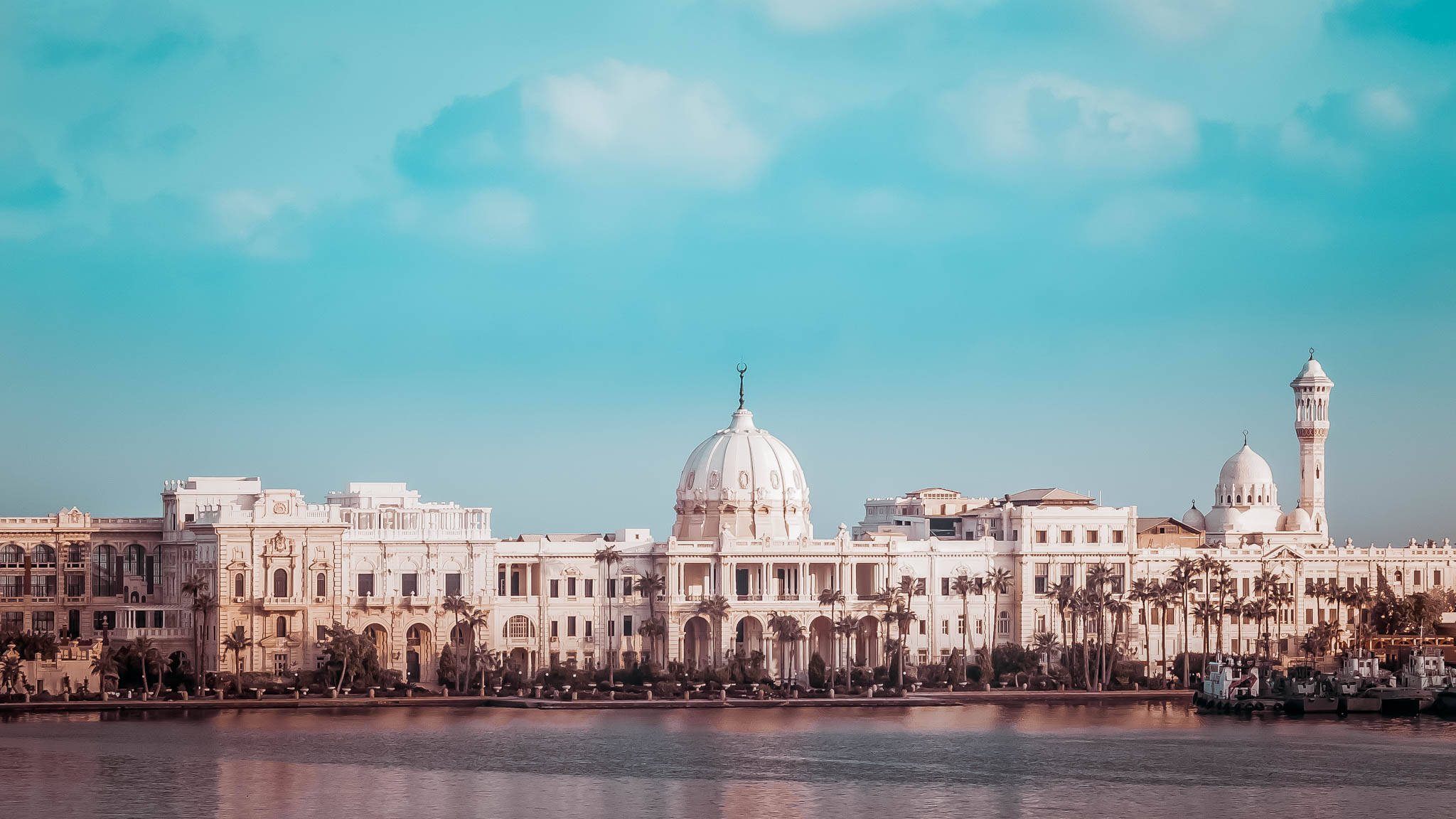 Alexandria 桌布 壁紙 — 宏偉的白色圓頂建築排列在平靜的海濱，上方是明亮的藍綠色天空，點綴著柔軟的雲朵。
