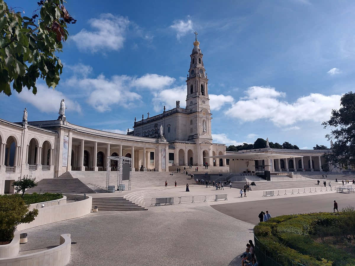 Portugal 桌布 壁紙 — 宏偉的白色石造大教堂，高聳的鐘樓矗立在明亮的藍天下，點綴著散落的雲朵，寬闊的台階上有遊客。