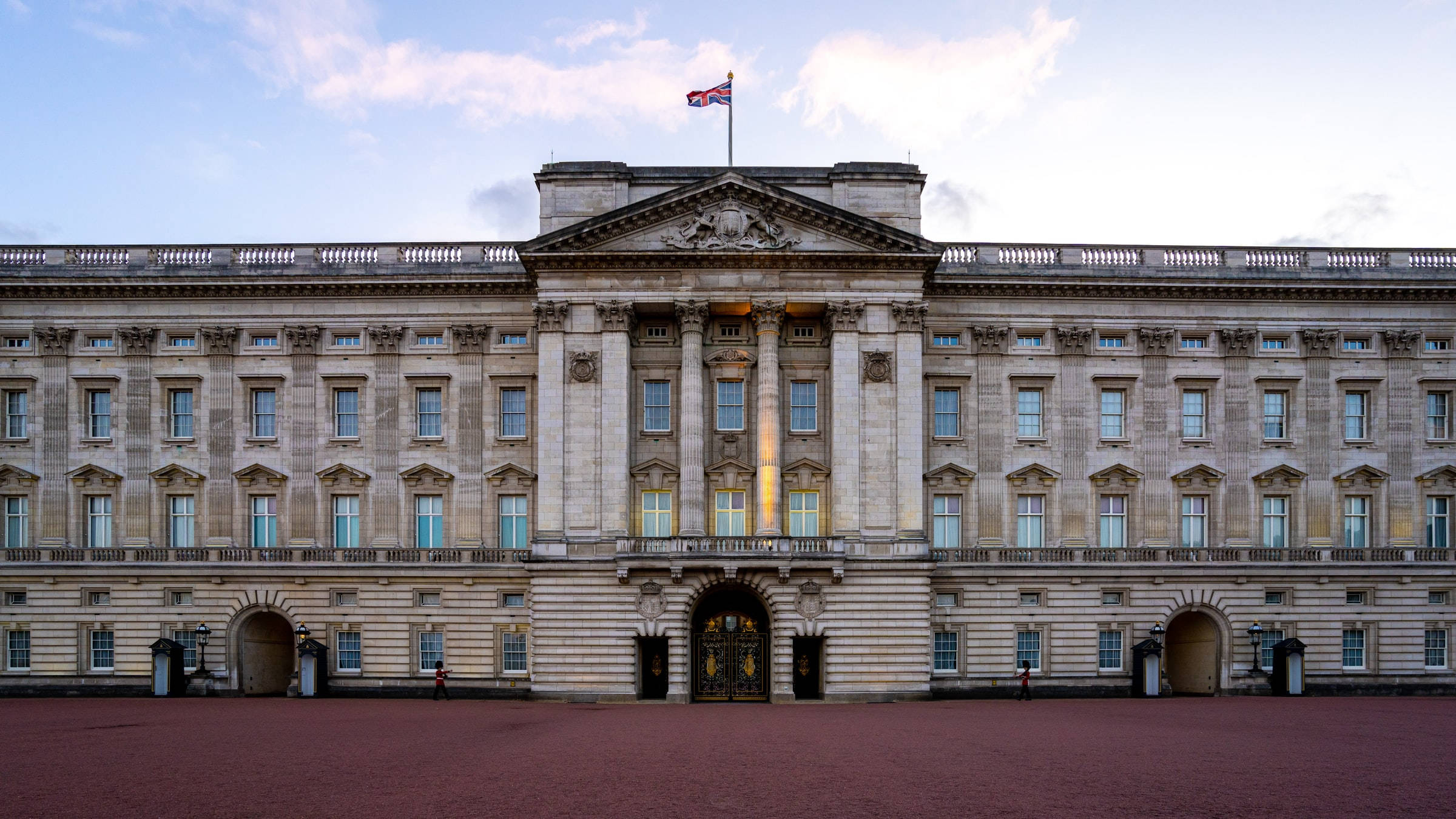 England 桌布 壁紙 — 宏偉的白金漢宮在柔和的暮色天空下巍然聳立，旗幟在華麗的外牆上方高高飄揚。