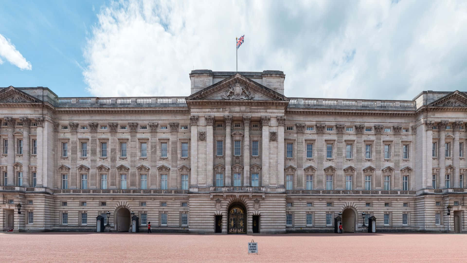 UK 桌布 壁紙 — 宏偉的白金漢宮在部分多雲的天空下巍然聳立，旗幟高高飄揚。