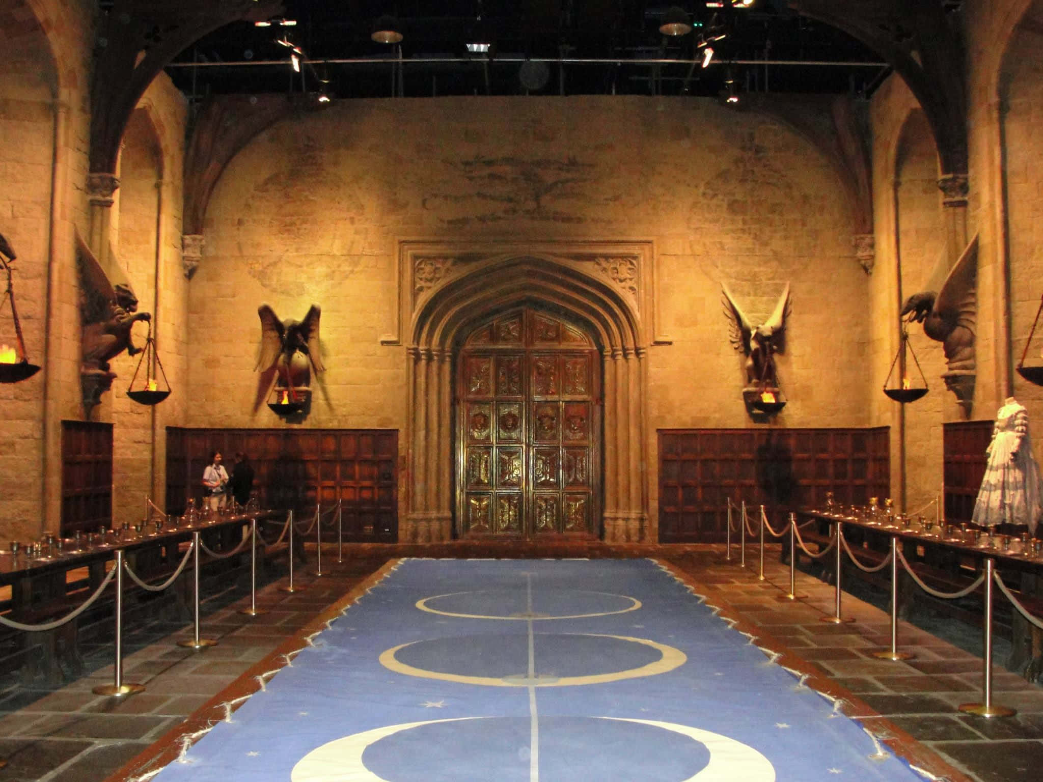 The Hogwarts Great Hall 桌布 壁紙 — 宏偉的石廳，藍色魁地奇球場上有圓環和星星圖案，在溫暖的燈光下。