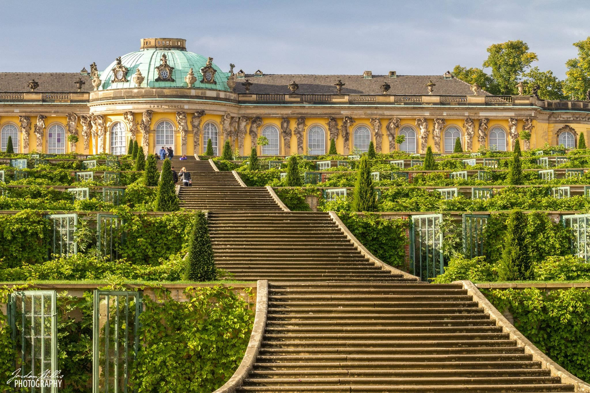 Potsdam 桌布 壁紙 — 宏偉的石階梯穿過茂密的綠色花園，通向一座雄偉的黃色宮殿，宮殿上有著綠松石色的圓頂，在清澈的藍天下。