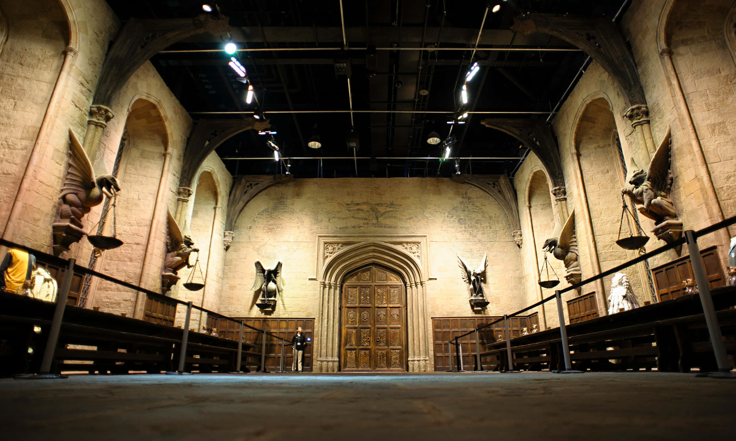 The Hogwarts Great Hall 桌布 壁紙 — 宏偉的石頭大廳，拱形天花板，天使雕像手持天秤，兩側是木門。