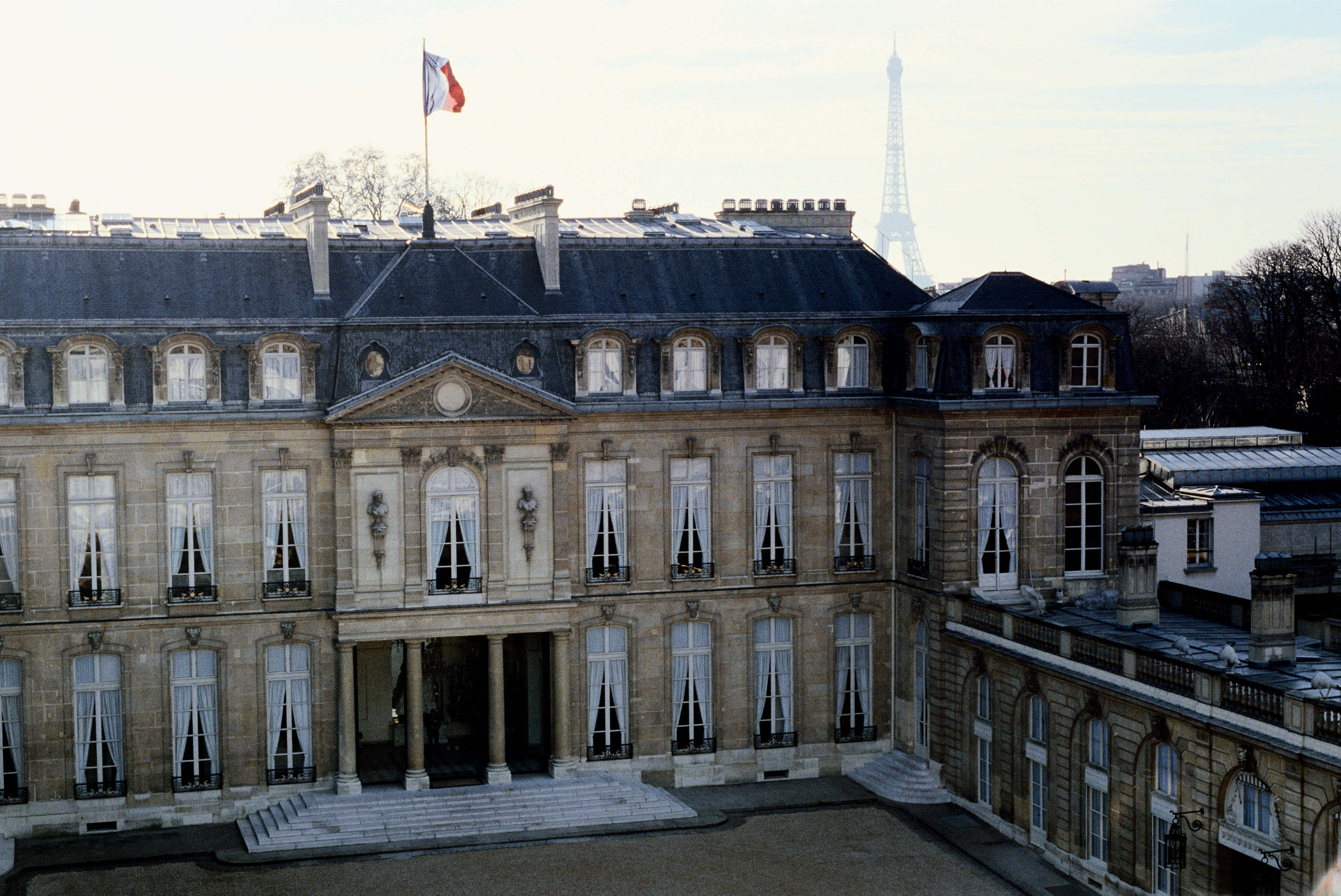 France 桌布 壁紙 — 宏偉的石頭宮殿，屋頂飄揚著法國國旗，背景中可見艾菲爾鐵塔，天空蒼白。
