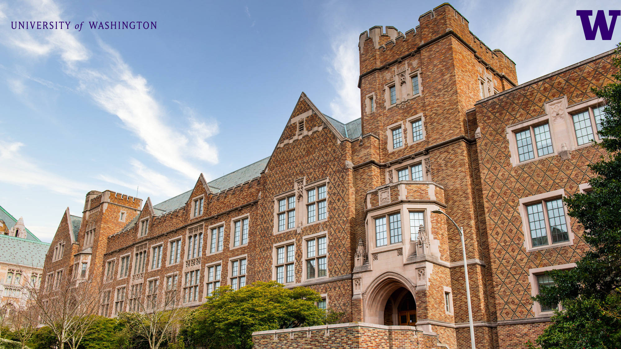 Building 桌布 壁紙 — 宏偉的磚造大學建築，設有塔樓和拱形窗戶，上方是明亮的藍天和縷縷白雲。