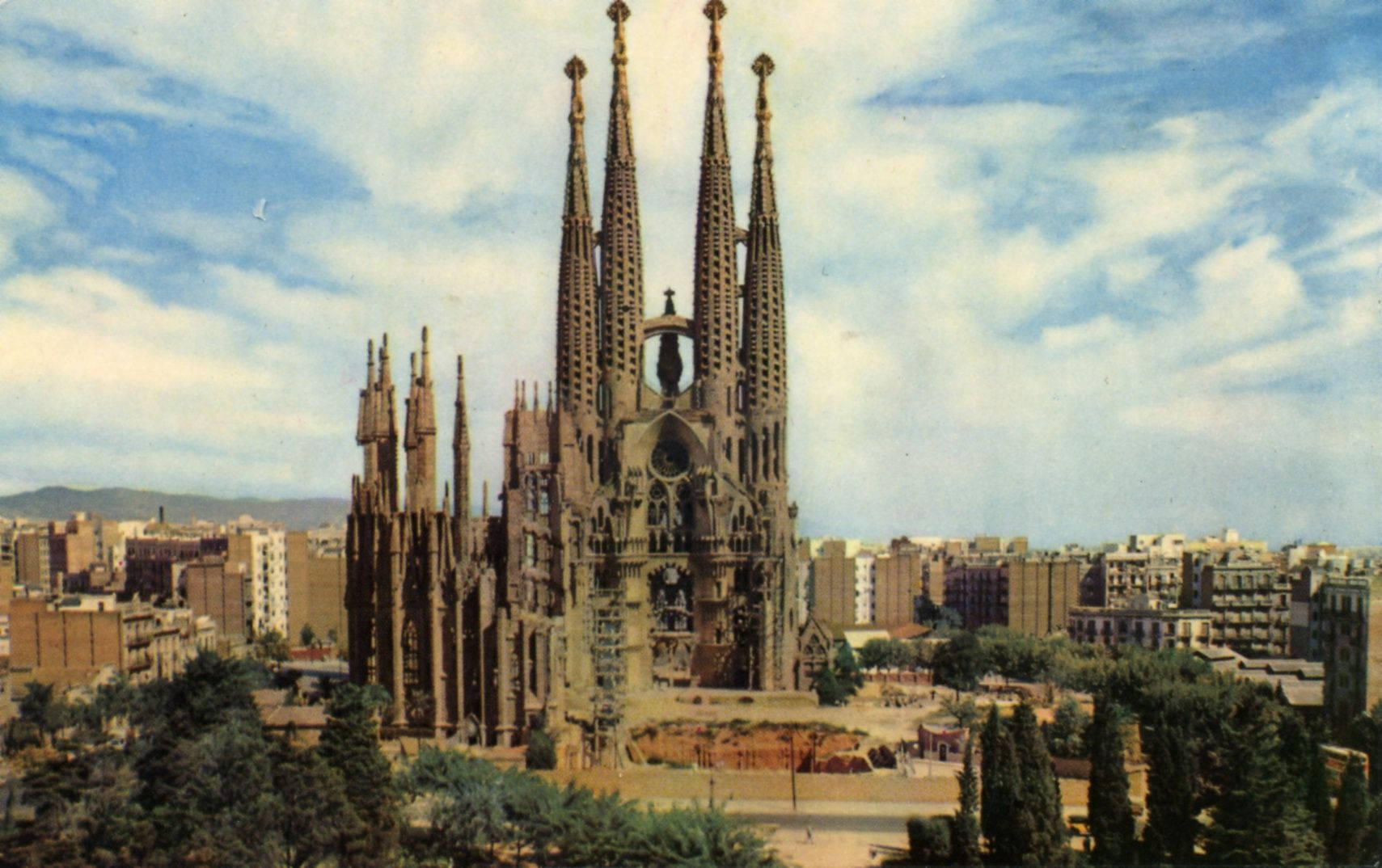 西班牙 桌布 壁紙 — 宏偉的聖家堂大教堂，高聳的尖塔在部分多雲的天空下，聳立在巴塞隆納的城市景觀之上。