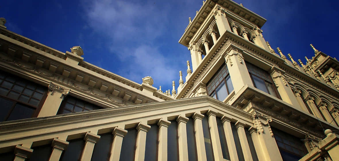 Buildings 桌布 壁紙 — 宏偉的裝飾性米色建築，帶有複雜的尖塔和柱子，在鮮豔的藍天下高聳入雲。