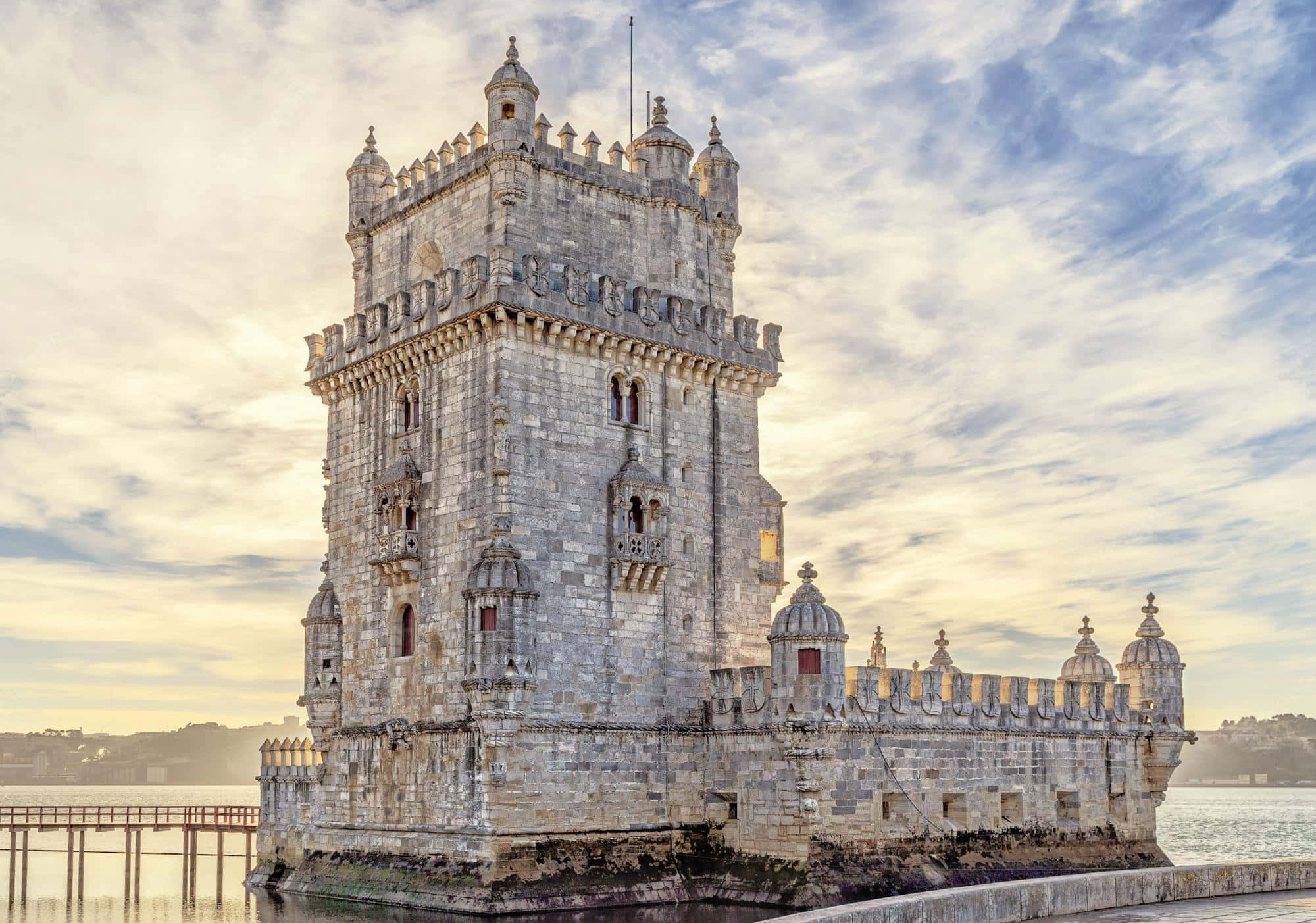 Portugal 桌布 壁紙 — 宏偉的貝倫塔矗立在水面上，天空是柔和的金色日落，散佈著雲朵。